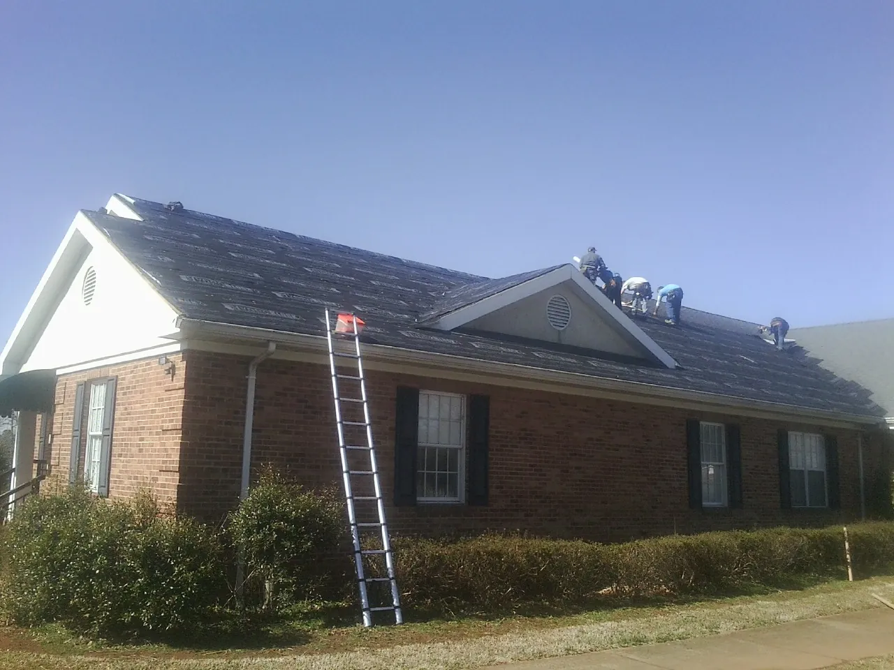 Crew tearing shingles off a brick ranch roof with a ladder set — Emergency Roof Repair work by our crew in Black Lick