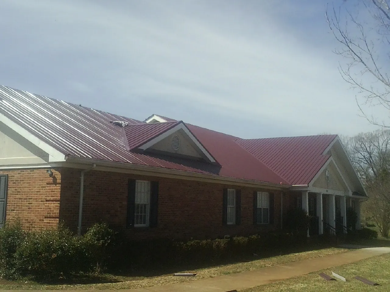 Red metal roof with gabled entries on a long brick building, from a Hail Damage Roof Repair job in Black Lick