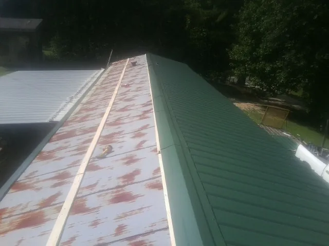 Old rusted panels beside newly installed green metal roofing — Wind Damage Roof Repair by Roofing Brothers in Black Lick