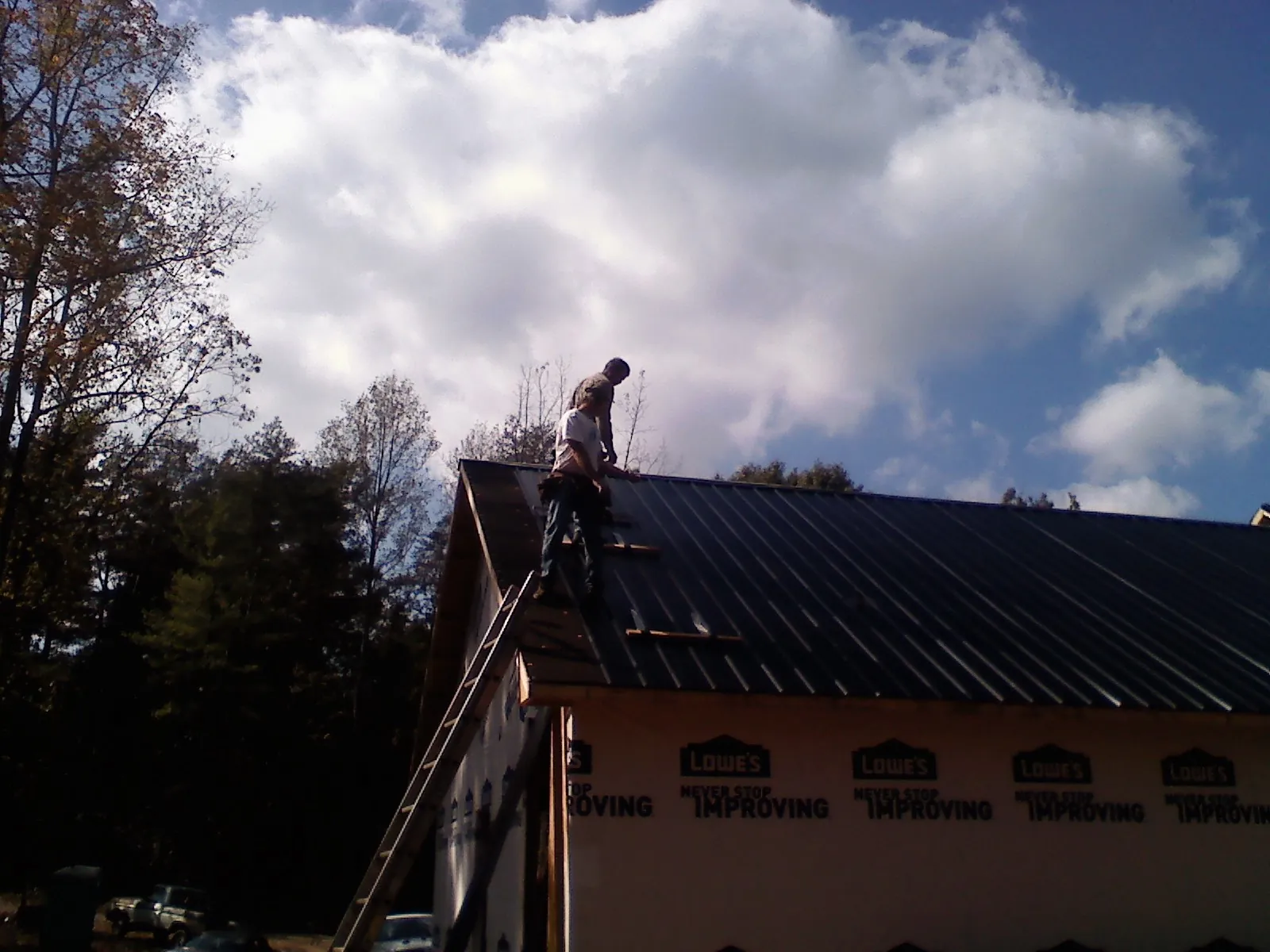 Roofer fastening dark metal panels high against a cloudy sky, from a Roof Inspection job in Black Lick