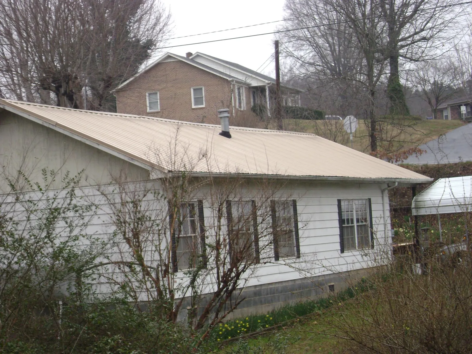 Tan metal roof on a white sided house set into a hillside — Commercial Roofing by Roofing Brothers in Black Lick