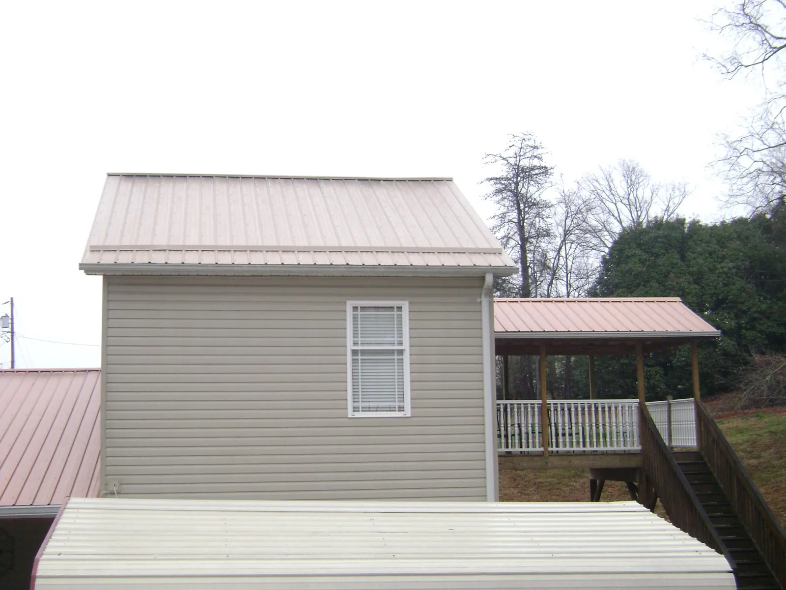 Tan metal roofs on a two story addition and attached porch, from a Roof Replacement job in Black Lick